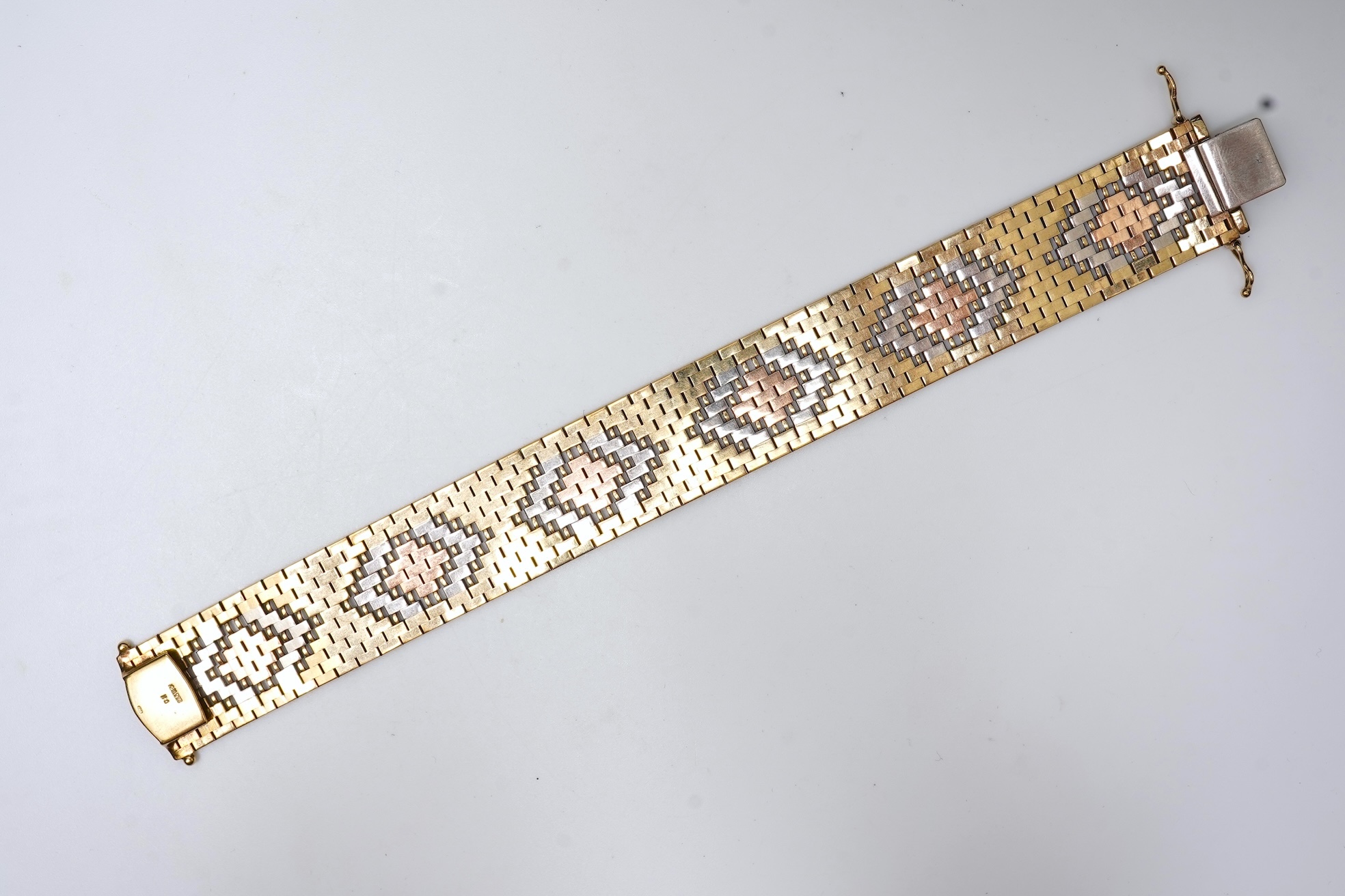 A gold bracelet, Italy, circa 1983, composed of brick linking with an engraved finish in tricoloured 9ct gold, length 18.5cm, Italian maker's mark, British import hallmarks, gross weight approximately 40.5 grams
